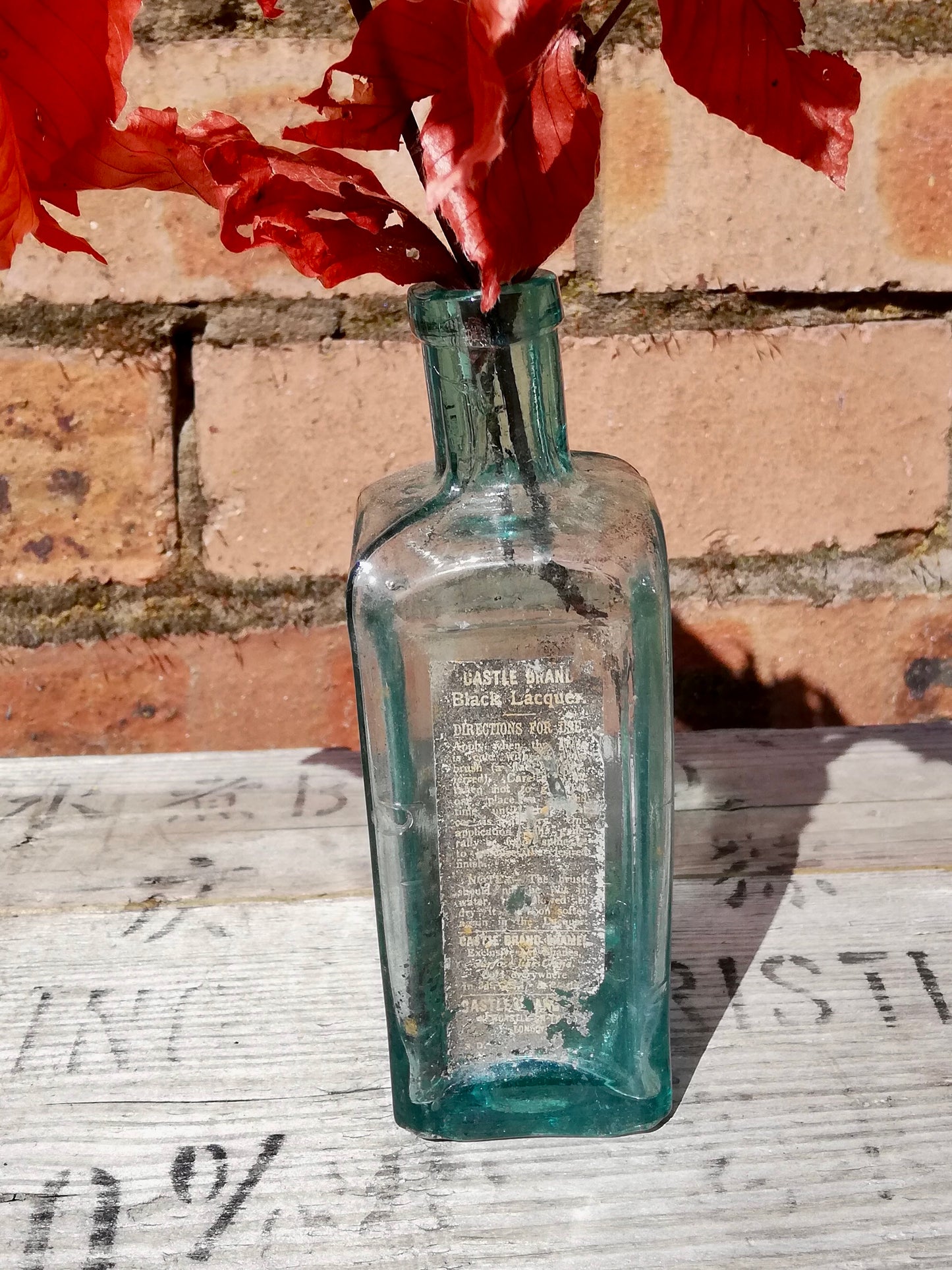 Vintage blue glass bottle bud vase with dried leaves