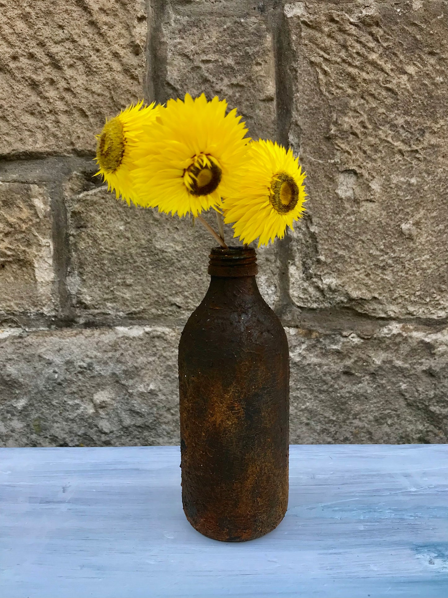 Bottle bud vase painted in layers of textured chalk paint in a rust finish comes with dried flower stems.