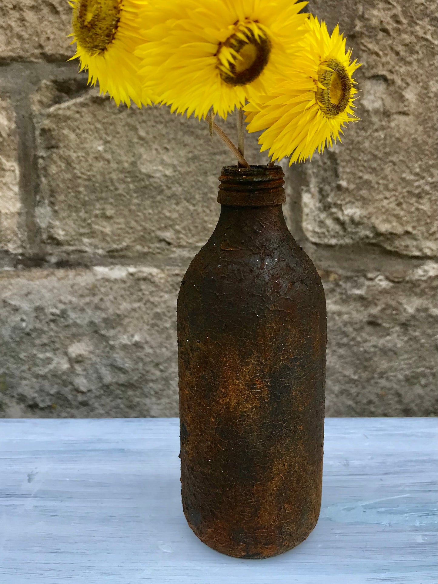 Bottle bud vase painted in layers of textured chalk paint in a rust finish comes with dried flower stems.