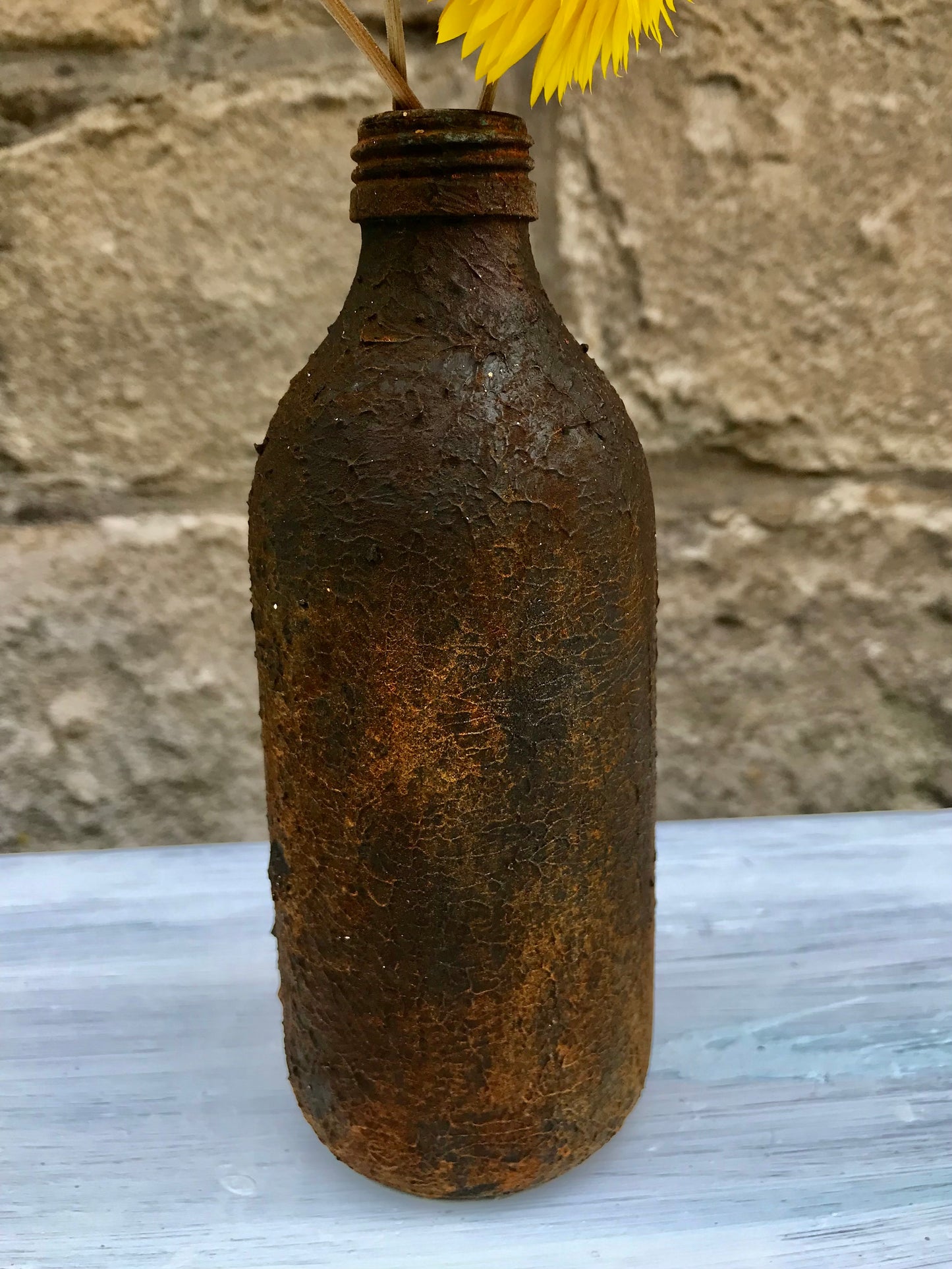 Bottle bud vase painted in layers of textured chalk paint in a rust finish comes with dried flower stems.