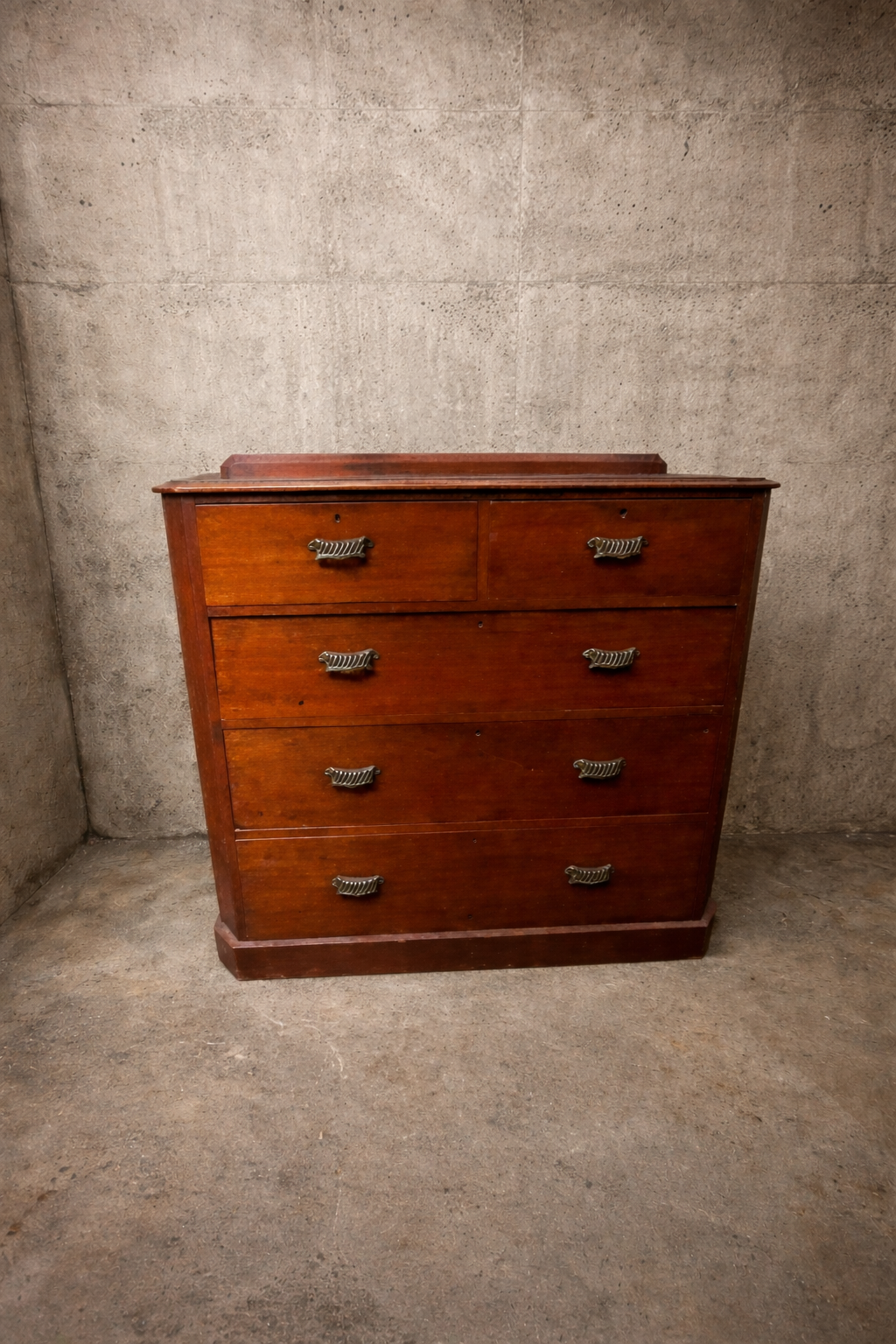 Wooden dresser with four drawers against a textured wall.